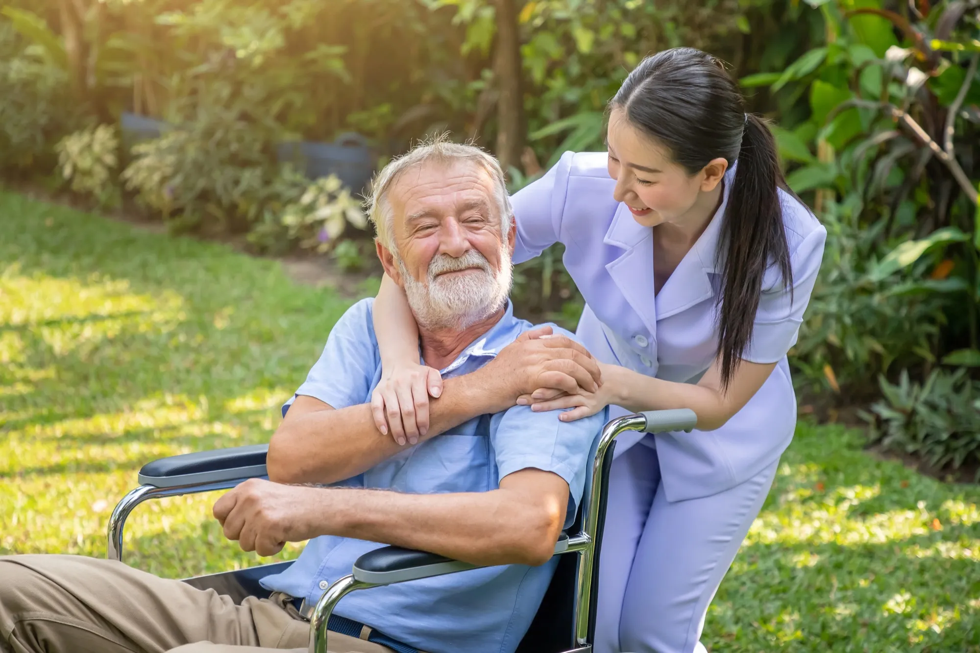 A carer with an older man in a wheelchair in a garden, both smiling
