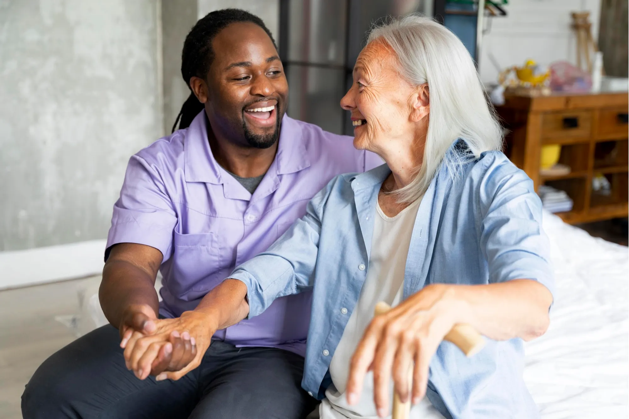 A carer laughing with an older woman as they hold hands
